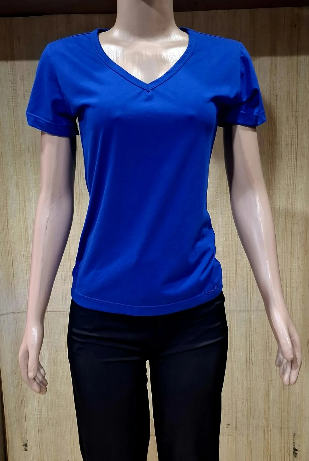 Manequim feminino com camiseta azul de gola em V e manga curta.