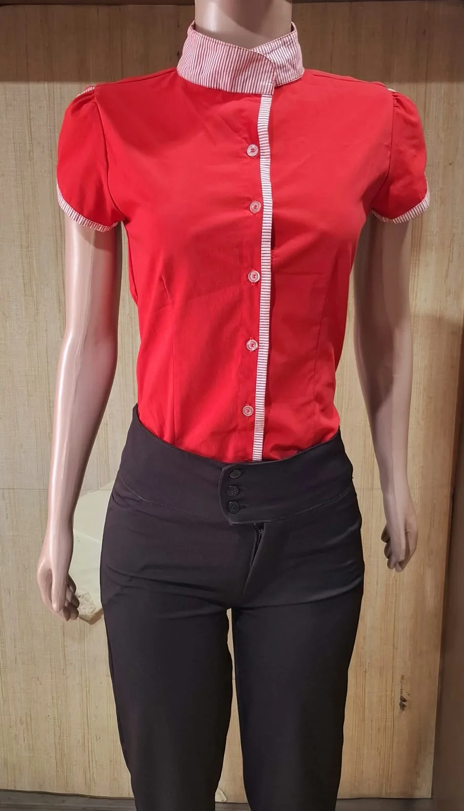 Manequim com camisa vermelha de gola alta listrada, abertura e punhos com detalhe listrado.