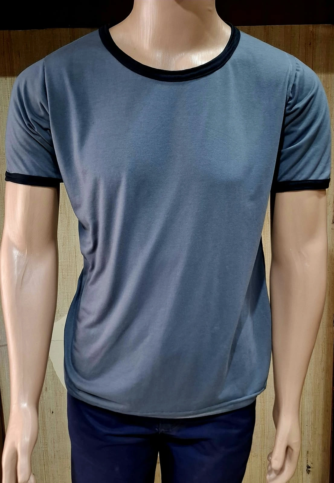 Manequim com camiseta cinza de gola redonda e acabamento preto na gola e nas mangas.