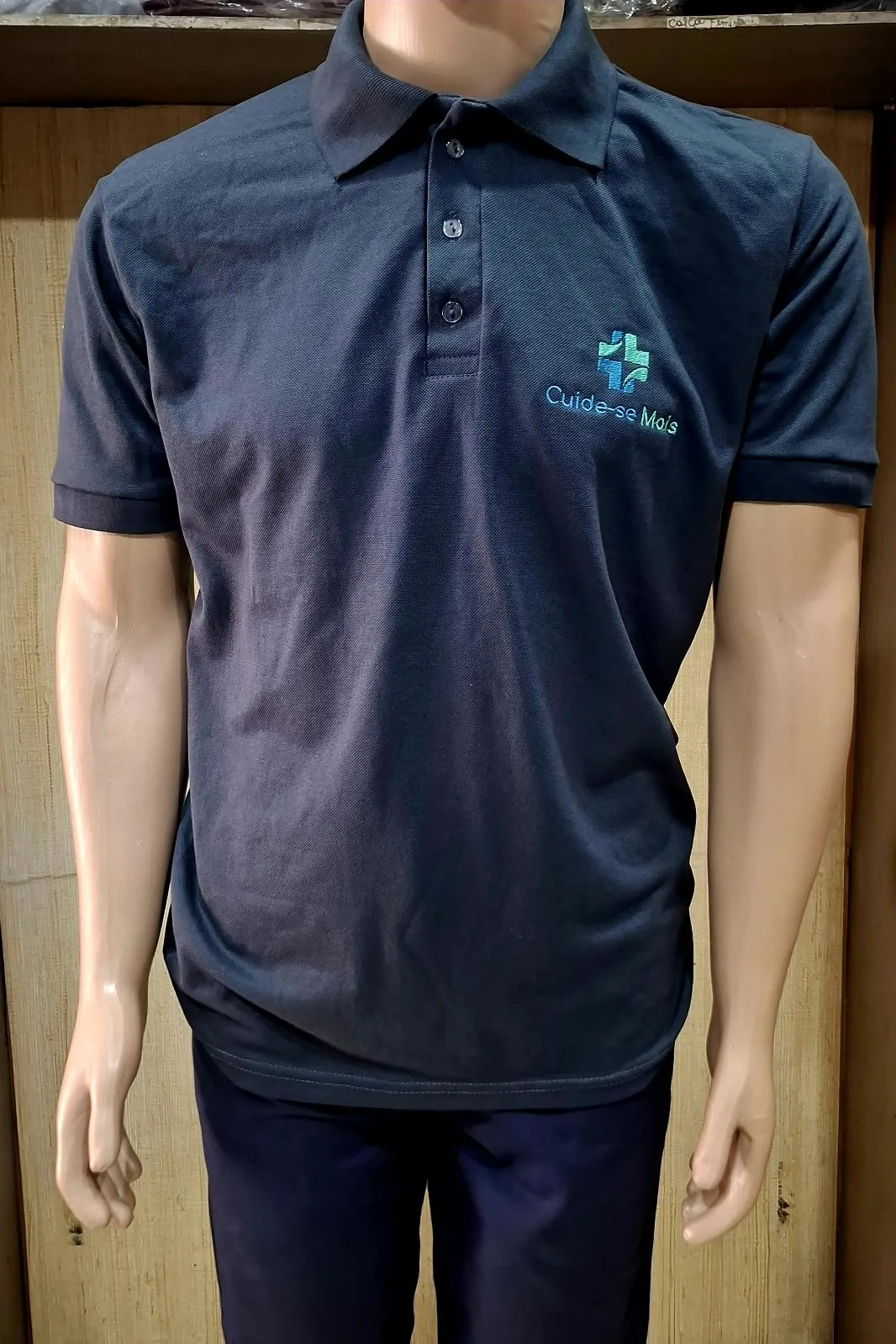 Manequim com camisa polo azul-marinho de manga curta e logotipo bordado Cuide-se Mais no peito.
