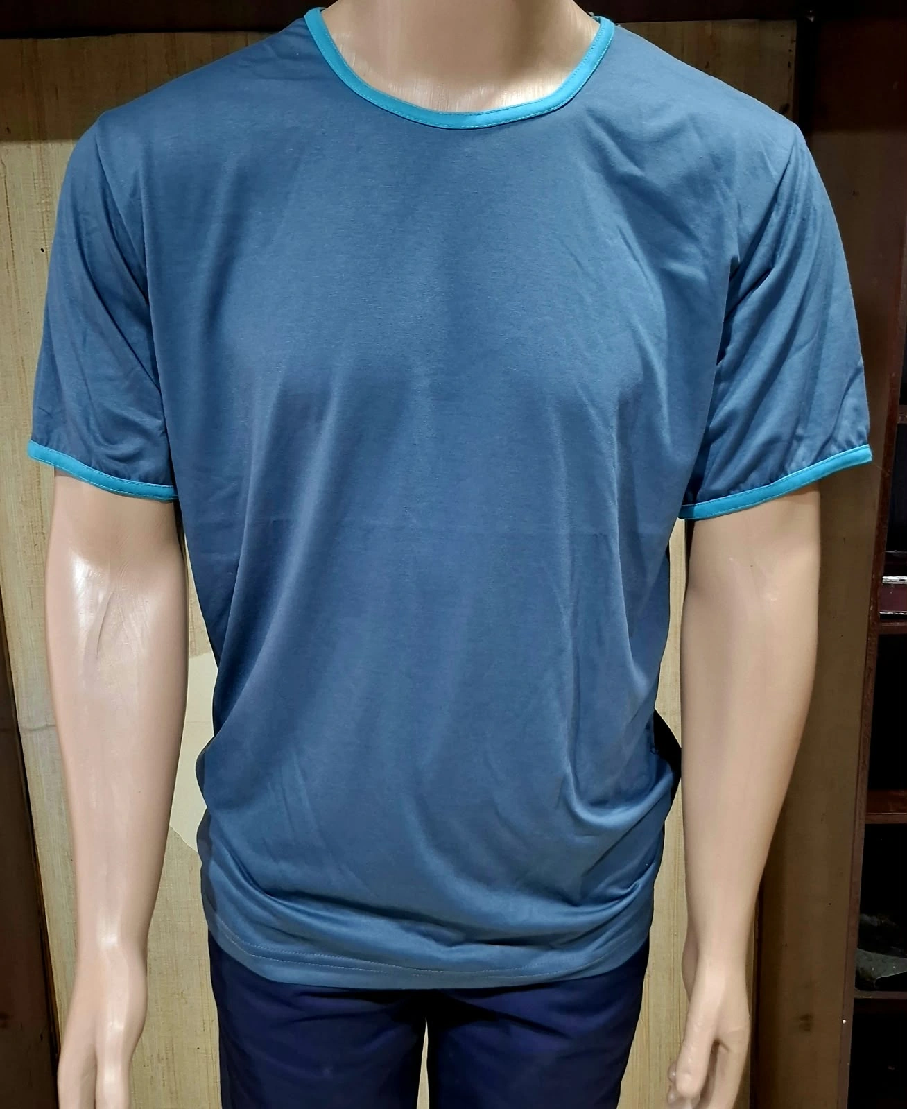 Manequim com camiseta azul de gola redonda e acabamento turquesa na gola e nas mangas.