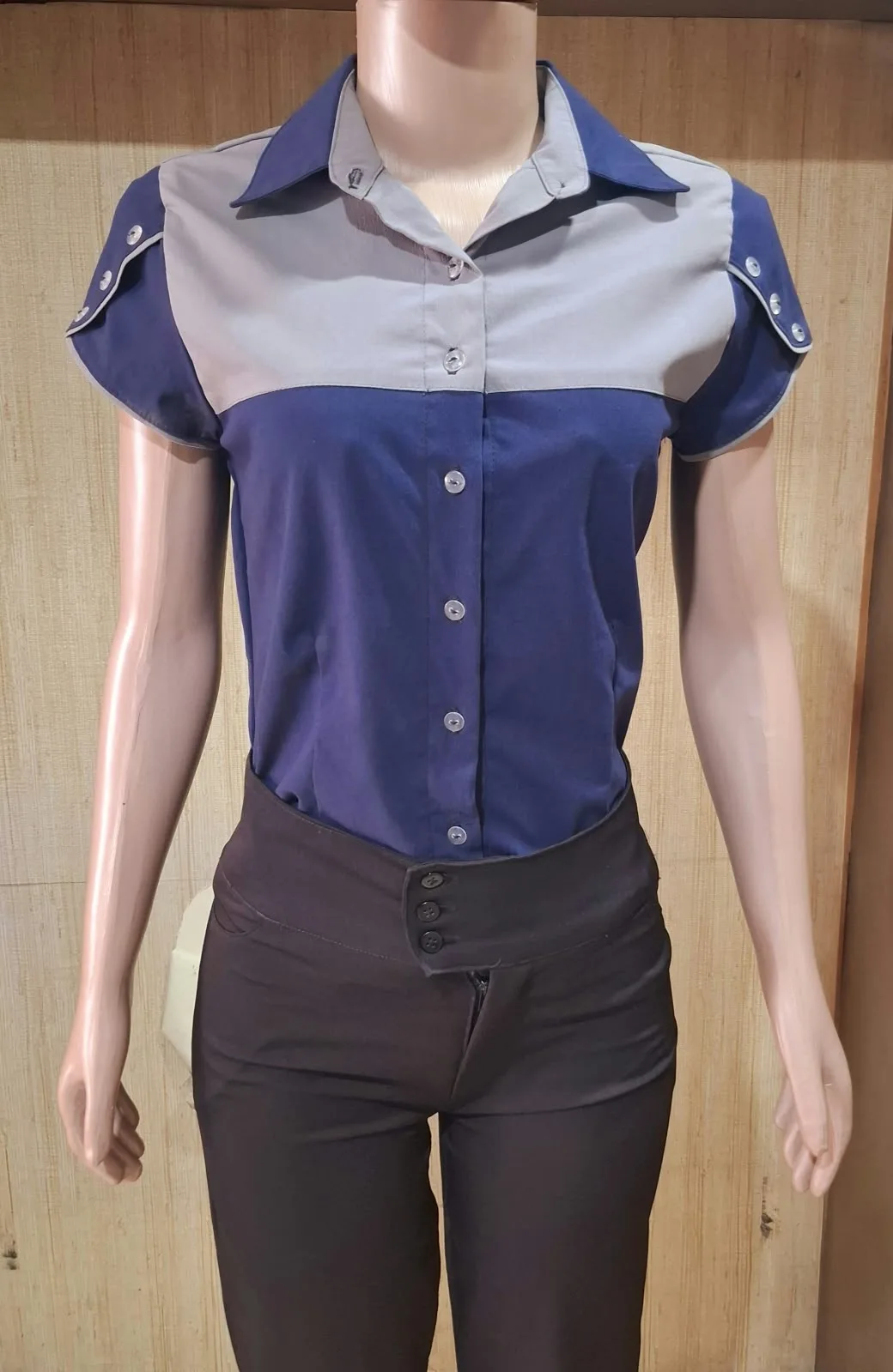 Manequim com camisa azul-marinho de manga curta, ombro em cinza e botões decorativos nas mangas.