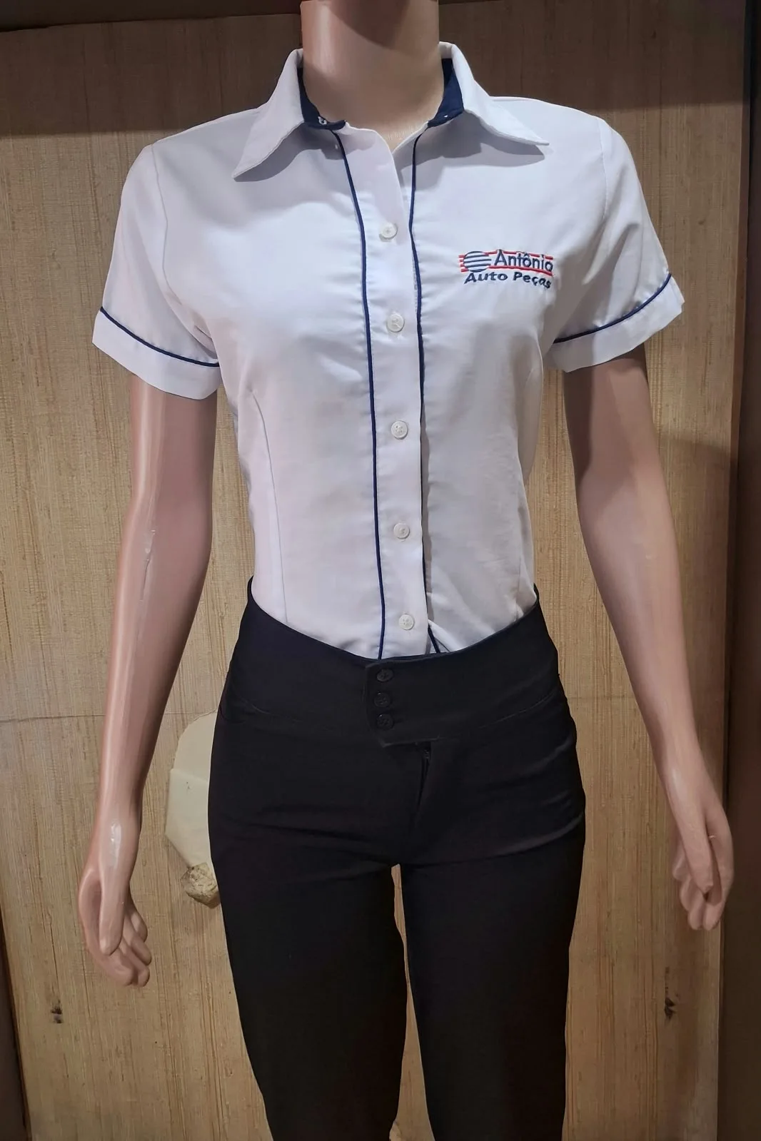 Manequim com camisa branca de manga curta, gola azul-marinho e logotipo Antônio Auto Peças no peito.